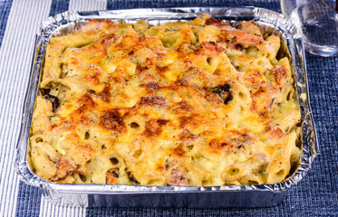 A family size take away Pasta Bake with melted cheese in a tin foil container