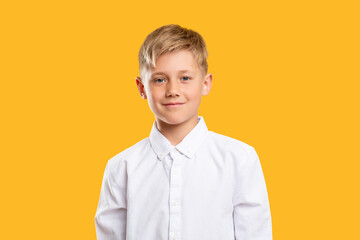 Happy kid portrait. Back to school. Confident blond boy in white shirt smiling isolated on orange background.