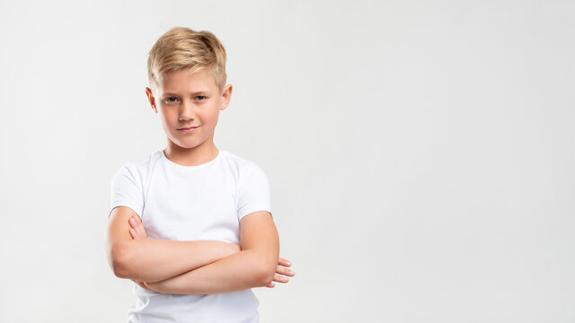 Confident boy portrait. Child lifestyle. Arrogant blond kid standing with crossed arms isolated on white copy space.