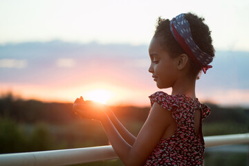 Photo at sunset. The child holds the sun in his palms. Against the background of the landscape....