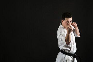 A karateka strikes or stands in a stance. Martial arts. Shidokan karate. Fighter in the studio. Kimono guy on a black background. Punch. Kick. World Karate Association the Shidokan. Black belt.