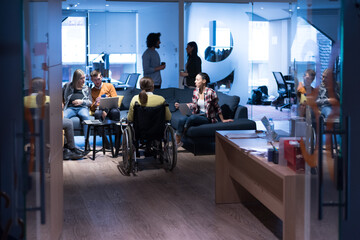 Fototapeta na wymiar Handicapped young woman with colleagues working in office. She is smiling and passionate about the workflow. Performing in co-working space. Office people working together.