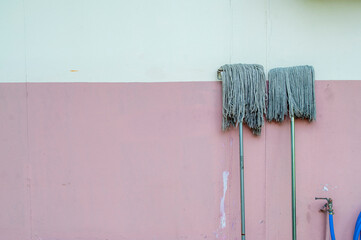 The old dirty mop was laid on the wall with a tap of water.