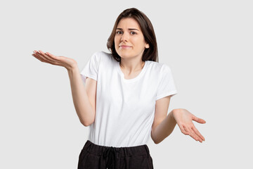 Confused woman portrait. Doubtful uncertainty. Clueless lady raising shoulders isolated on neutral background.