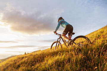 Female mountainbiker riding on a trail in the mountains - obrazy, fototapety, plakaty