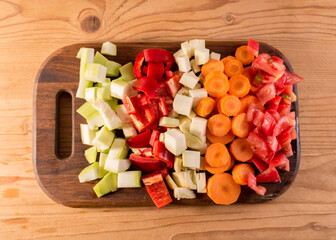 Close up sliced vegetables in a wooden cutting board. Slices of carrot, tomatoes and squash.