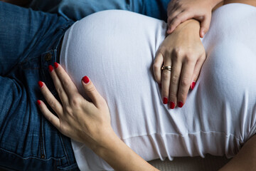 Hands of mom and son on a pregnant belly. Woman in a white T-shirt. Red manicure. A tender moment...
