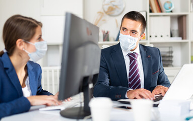 Portrait of businessman wearing protective face mask working in office with female colleague. Pandemic precautionary concept