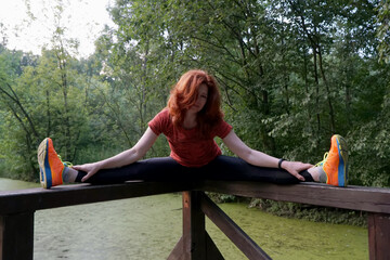 slender athletic lady stretches her muscles on the shore of the pond