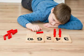 Boy lying on the floor and playing counting game "insert a stick ". Play and learn. Mathematical tasks. Basic addition and subtraction.