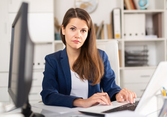 Portrait of busy female entrepreneur sitting at office desk with papers and laptop ..