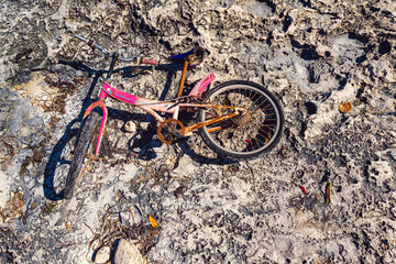 Rusty pink bicycle lying on stones of ocean coast