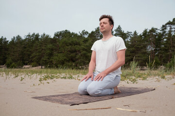 Naklejka na ściany i meble Young caucasian man preparing for yoga practice sitting on the beach