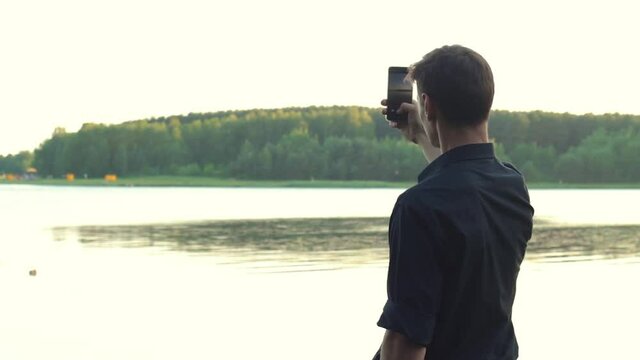 guy in a black shirt stands on the lake and takes a vertical photo on the phone