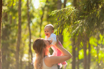 Young mother holding daughter in her arms. mom kisses and plays with daughter in the summer. Happy family in the park.
