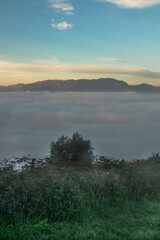 Landscape of a sea of clouds in a Spanish sunrise with the mountains in the background and the grass of a meadow in the foreground.