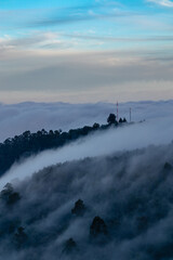 The fog covers a forest covering the trees and the antennas on the hill