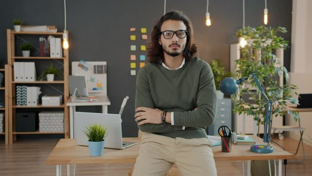 Portrait of serious young businessman looking at camera standing in office in the evening. Modern business, ambitious people and workplace concept.