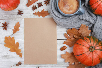 Craft paper for text, coffee cup wrapped in plaid, spices, oak leaves, acorns, orange pumpkins on white wooden table. Autumn drink concept. Fall, pumpkin spicy latte, thanksgiving, top, copy space