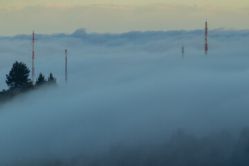 Fototapeta na wymiar The fog covers a forest covering the trees and the telecommunication antennas on the hill