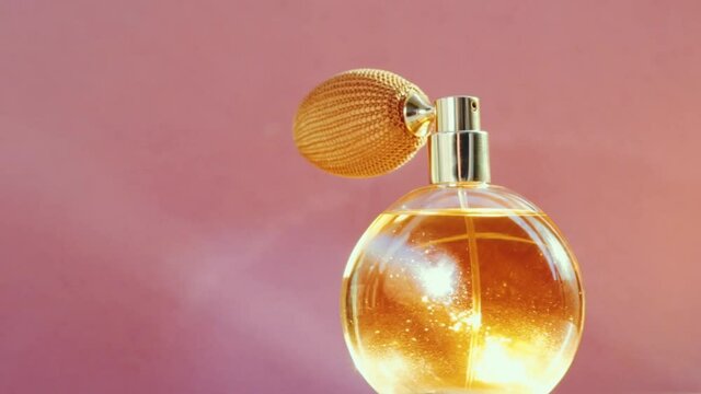 Luxury golden perfume bottle and shining light flares on pink background, glamorous fragrance scent as perfumery product for cosmetic and beauty brand, stock footage
