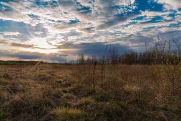 Clouding sunset in a field in a village in Belarus. Evening time in the field. The sun behind the clouds. The sun through the clouds. Shining sky.