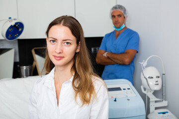 Obraz premium Portrait of young woman client of beautician sitting in clinic waiting for procedures, man doctor on background