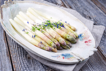 Traditioneller gekochter weißer Spargel mit violetten Köpfen garniert mit Kräuter und angeboten...