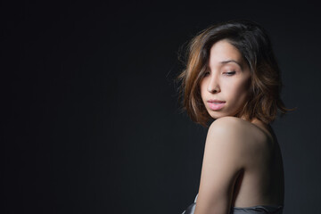 Naklejka premium Portrait of a beautiful young girl on a dark background in a gray silk dress. The concept of beauty, youth and naturalness