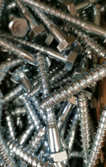 New shiny iron steel bolts lie in a heap. Textured background. Stainless screws close up. Connection, kind. Selective focus