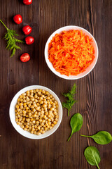 Vegetarian meal. Chickpeas and carrot in bowls on dark wooden table top view