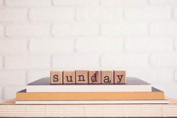 The word SUNDAY, alphabets on wooden rubber stamps on top of books with bricks background, blank copy space, vintage minimal style. Concepts of day, weekend, break and holiday.