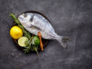 Dorado fish in the wooden plate  on black background with  rosemary and citrus.