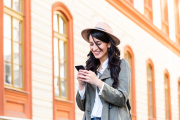 Fototapeta premium Photo of a woman using smart phone. Beautiful woman texting on the street. Beautiful woman spending time in the city. Fashionable woman with smart phone