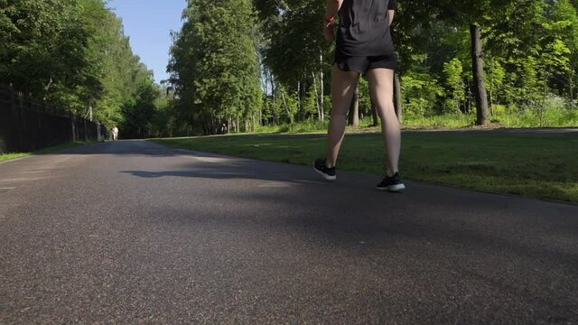 girl bun on her head without makeup black T-shirt walks fast breathes through her mouth in park listens music wireless headphones early morning takes care playing sports active class healthy lifestyle