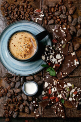 Cup of espresso coffee with jug of milk, handmade dark chocolate, coffee and cocoa beans around over dark ceramic tile as background. Flat lay, copy space