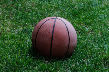 Basketball ball on the grass. Basketball ball waiting for children. Green grass and worn basketball ball.