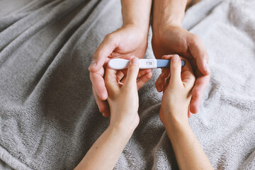 View from the top of female and male hands holds a positive test for pregnant