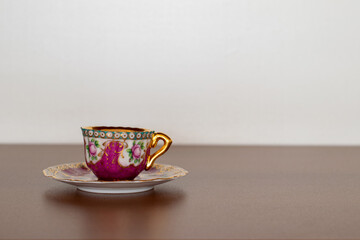 small cup and painted saucer, with blurred background and space for text.