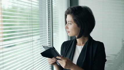 Portrait of young business woman in office talking on phone and smiling. Beautiful entrepreneur looking at the window and waiting for delivery man. Concept of technology, communication.