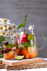 Infused water with fruits, berries and mint in glass pitcher against the grey background