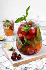 Infused water with fruits, berries and mint in glass pitcher on the white wooden table. Healthy nutrition drink