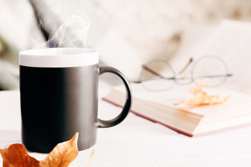 Autumn cozy composition. Plaid, steaming cup of hot chocolate, book, autumn leaves. Autumn or winter concept of coziness and interior. Front view, copy space