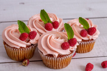 Cupcakes with delicate pink cream on a white wood background decorated with raspberries and a mint leaf.