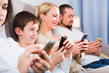 Modern young family sitting with smartphones in home interior