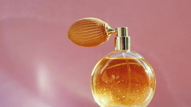 Luxury golden perfume bottle and shining light flares on pink background, glamorous fragrance scent as perfumery product for cosmetic and beauty brand, stock footage