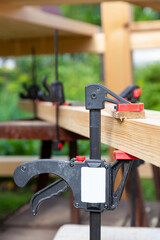 Several clamps on wooden beams and timber during the construction of a black metal arbor in a summer cottage on the background of green grass on a summer day.