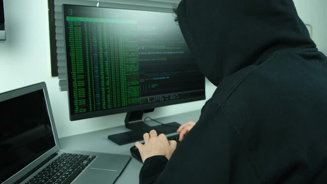 masked hacker using computer to hack data organizing massive data breach attacks on corporate servers located in a secret underground place wearing a black hoodie black cap and a scarf hidde identity