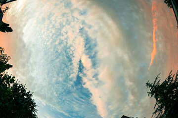 Dramatic fish eye view of textured and colorful clouds in the sky during sunset