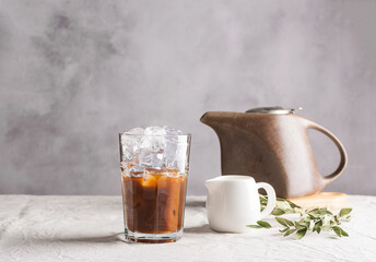 Cold black coffee with ice cubes and milk in tall glass. Refreshing coffee drink on the table gray...